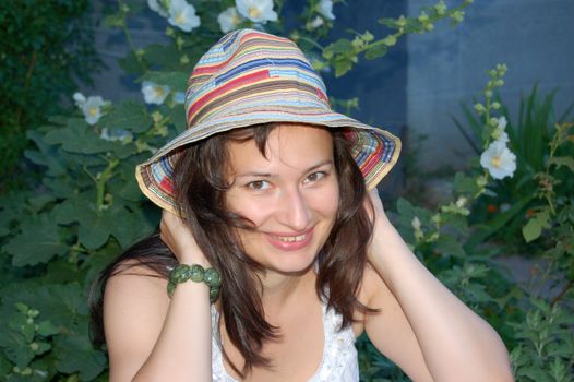 close-up of attractive young brunette in colorful hat against green leaves in the garden