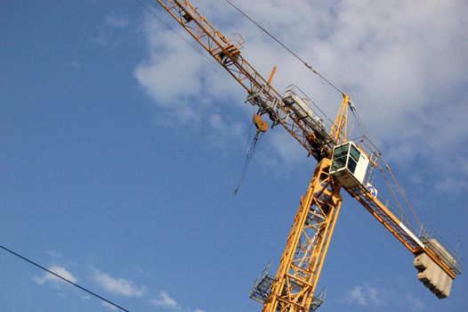 yellow lifting crane over blue sky with clouds