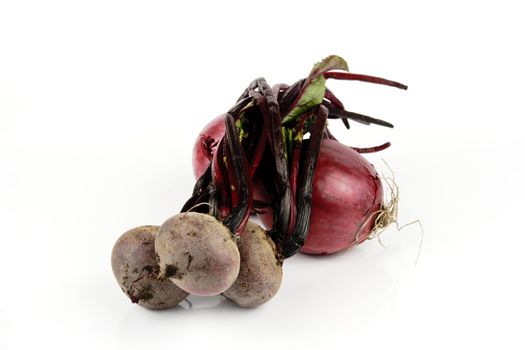 Two raw unpeeled red onions and a bunch of beetroot on a reflective white backgrounds