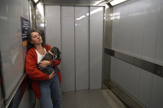 The lonely woman in a cabin of the lift with the puppy on hands