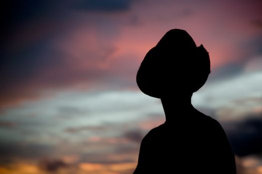 Woman in a cowboy hat silhouetted against a colorful sunset sky.
