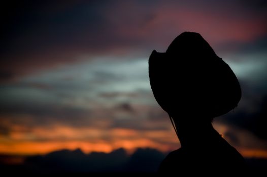 Woman in a cowboy hat silhouetted against a colorful sunset sky.