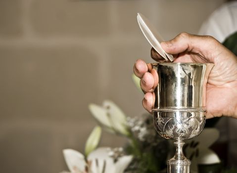 Priest's hand holding holy bread and chalice during Mass