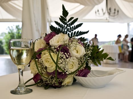 Bride's flower bouquet on table next to glass of wine
