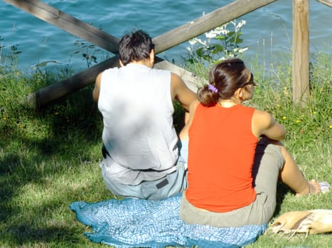 Young couple relaxing on the grass in the park, in front of the lake