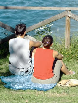 Young couple relaxing on the grass in the park, in front of the lake