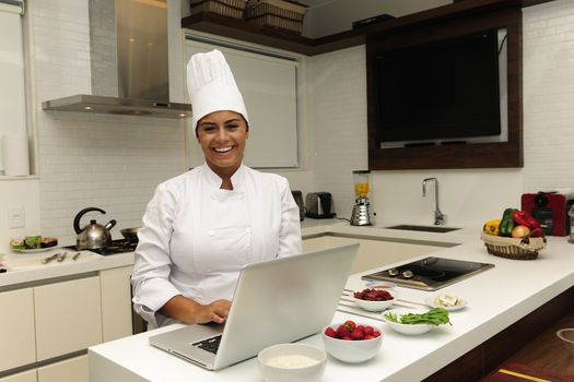 Happy chef cooking in kitchen and using laptop