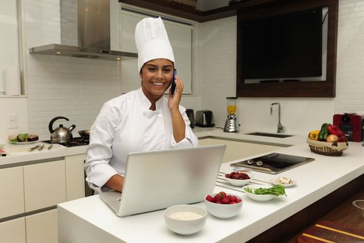 Chef cooking in kitchen talking on phone and using laptop