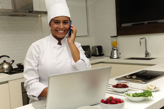 Chef cooking in kitchen talking on phone and using laptop