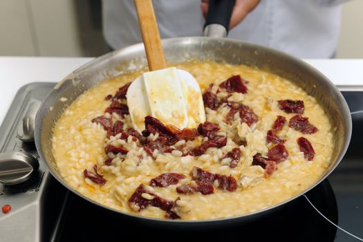 Chef cooking risotto with dried tomato stirring