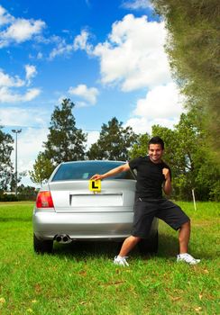 Excited male driver holding licence plates to rear of silver motor vehicle.  He is smiling and making a victory fist.