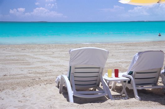 Empty deck chairs wait on a white sandy beach facing the turquoise waters of the Bahamas.