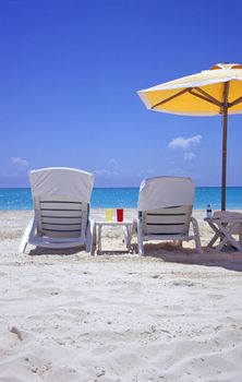 Empty deck chairs wait on a white sandy beach facing the turquoise waters of the Bahamas.