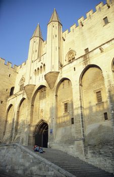 A couple stits on the steps of the Palace of the Popes as the sun goes down. Avignon, France.