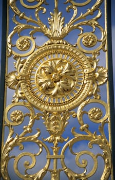 Detail of golden fence ironwork on a blue sky background.