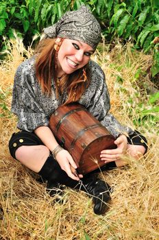 beautiful pirate girl is holding a knife and wooden chest, she is sitting  in the dry grass