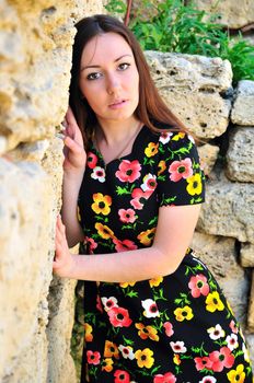 beautiful brunette standing close to the ancient stone wall, she is wearing flowered dress