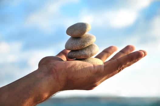 balancing stones  in man's palm over blue sky