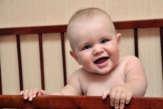 funny baby holding bed grating and smiling