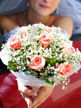 bride is sitting in the car and holding wedding pink flowers