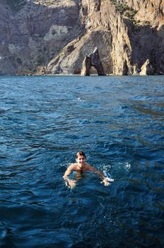 happy man is swimming  in open sea near Karadag Gate  in Crimea