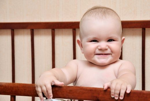 funny baby holding bed grating and smiling, hey first tooth is visible