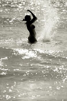 silhouette of a wet young woman in a waving sea splashing the water, vertical