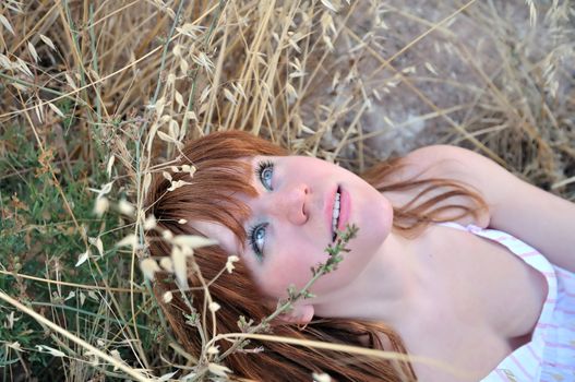 redhaired beautiful girl laying in the dry grass and looking up