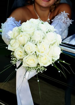 bride is sitting in the car and holding wedding white flowers