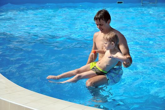 father teaching his little son to swim, they are smiling, they are happy 