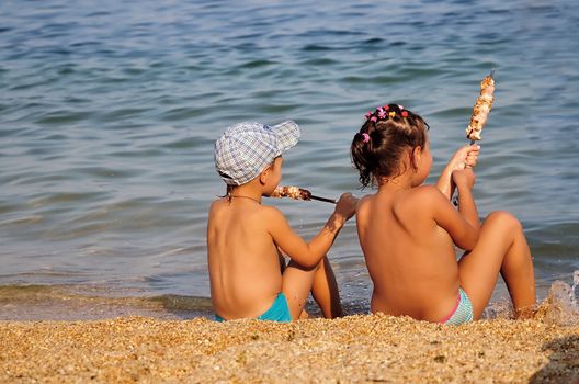 children eating  shashlik  on the shore of  sea