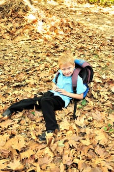 Child resting in a park amongst autumn leaf fall after school