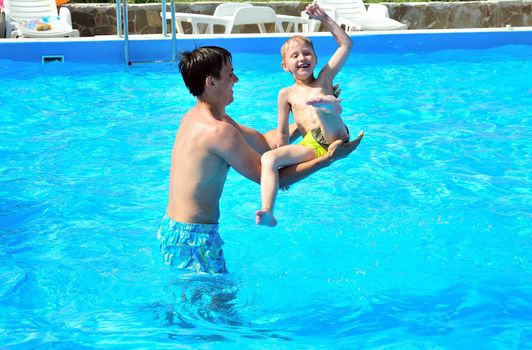 father fling in  his little son in the pool, they are smiling, they are happy