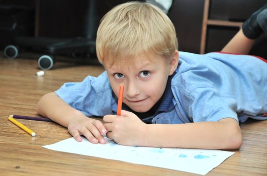 little boy drawing using  pencils, he is laying on the flour
