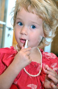 Little girl using lipstick, she is wearing necklace