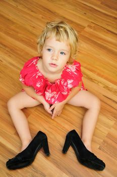 little girl is sitting on the flour, she is wearing mother's high-heels shoes, snappy dresser