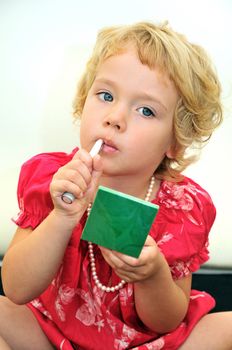 little girl using lipstick and powder, she is wearing necklace