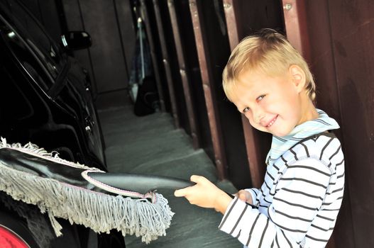 Young boy cleaning his dad's dark car in 	 garage