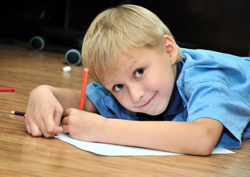 little boy drawing using pencils, he is laying on the flour
