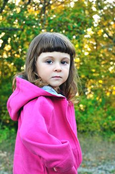 little girl  in the forest in fall time looking at the camera.