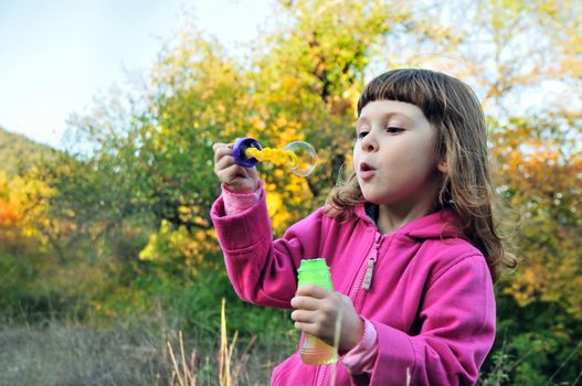 little girl blowing soap bubbles to 	 windward in the forest