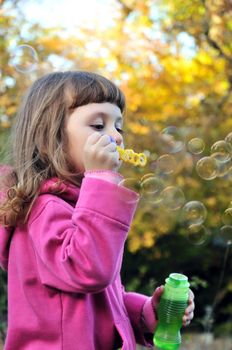 little girl blowing soap bubbles in autumn forest