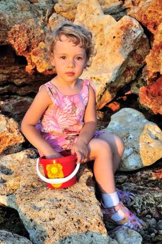 little girl is playing with can  on the cliffed beach