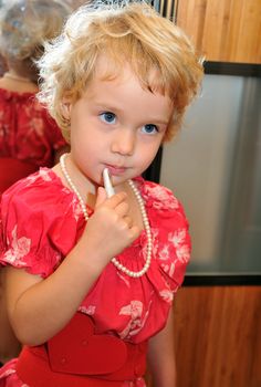 Little girl using lipstick, she is wearing necklace