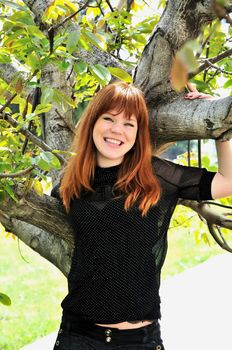 redhaired girl is standing under the tree and smiling