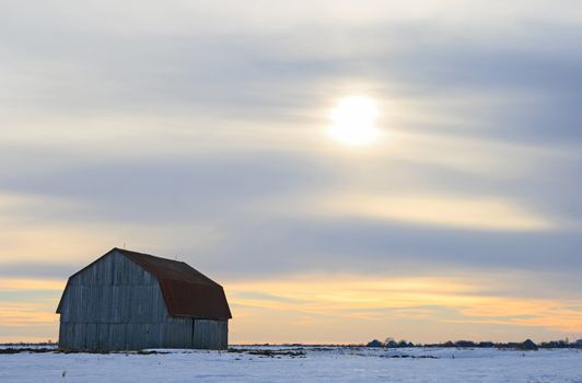 Old wooden barn in a snowy field in the evening.