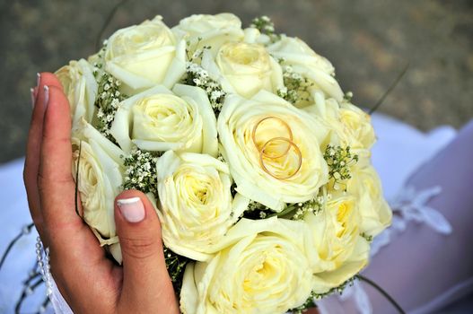 bride holding wedding flowers (roses) and gold rings 

