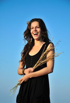 laughing brunette girl over blue sky holding dry 	 spikelets