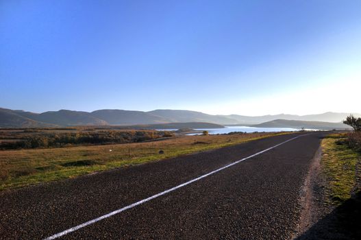 country road between lakes and autumn forest