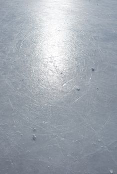 Surface of an outdoor ice rink replete with skate marks reflects the sun.